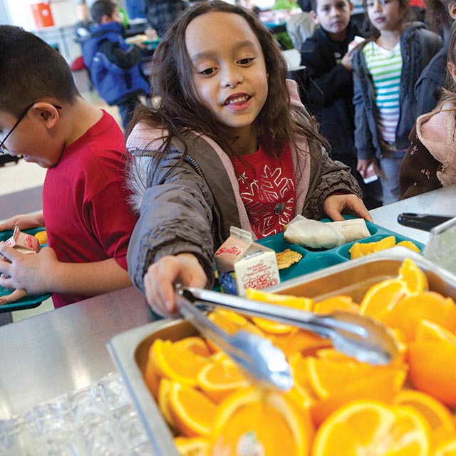 A kid selects an orange wedge with tongs