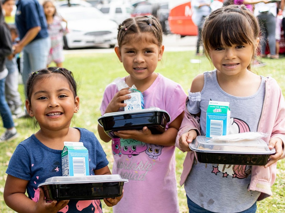Young girls in a community park smile with picnic lunch
