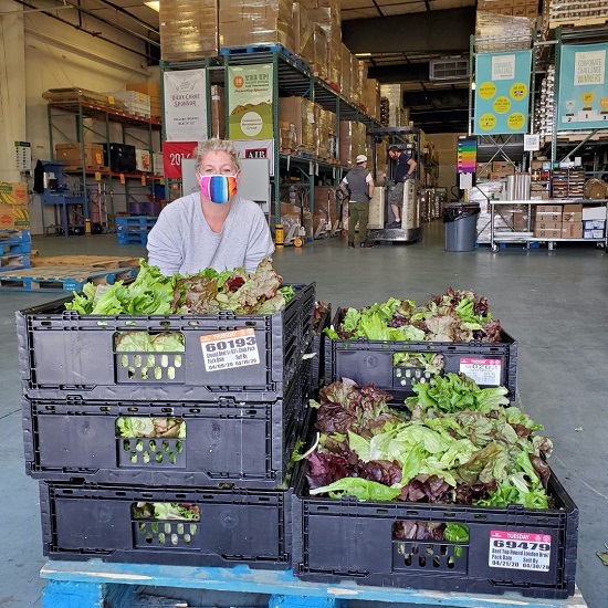 A woman poses with a pallet of lettuce at a food bank