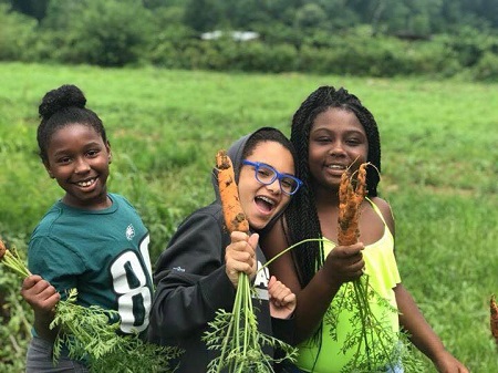 Girls smile while holding carrots on a farm.