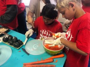 Children cut avocados and carrots for a salad.