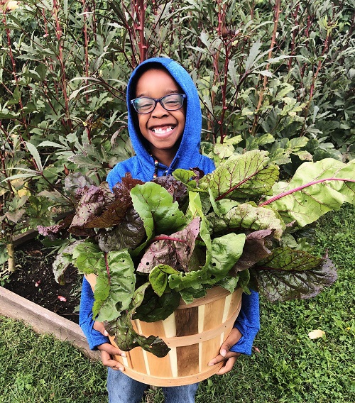A student smiles with a full basket of fresh chard.