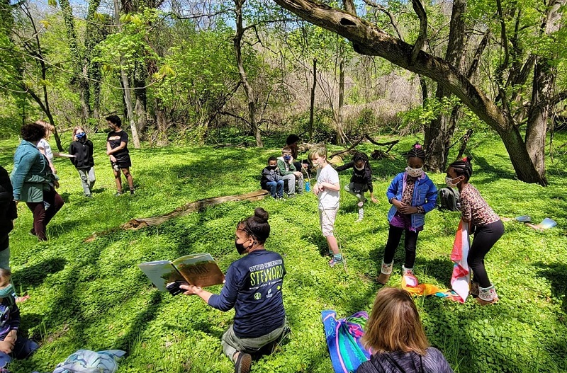 A teacher reads children a book out in the forest.