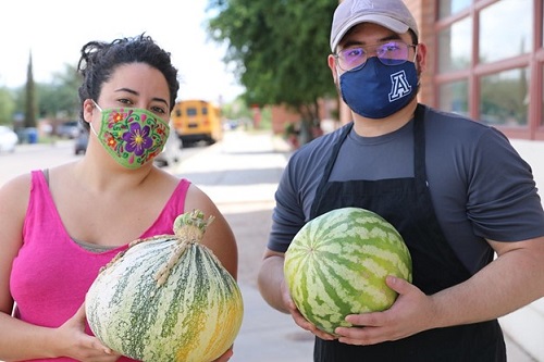 Two adult volunteers hold ripe produce outside of the school garden