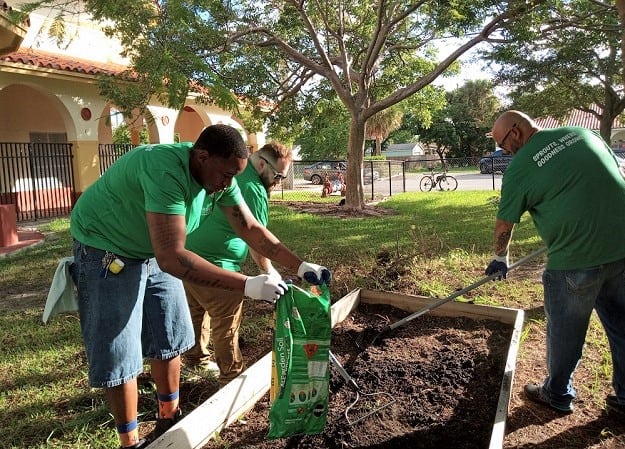 Three men add soil to a garden bed and smooth it over with a rake.