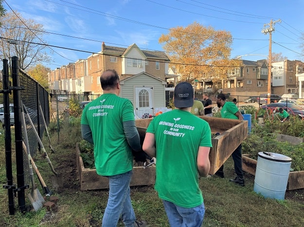 Volunteers carry a wooden garden bed across grass.