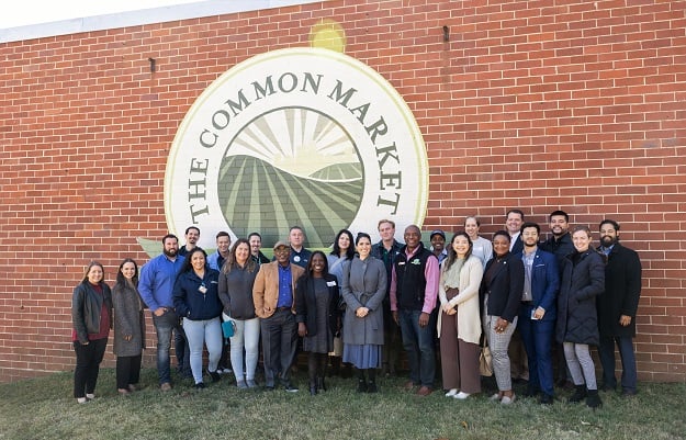 A group of people stand outside of a brick building and pose for a photo.